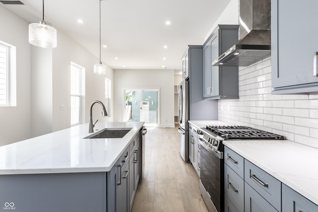 39 N Walcott St, Indianapolis, IN 46201 - kitchen with stainless steel appliances, a sink, wall chimney range hood, light wood-type flooring, and a kitchen island with sink