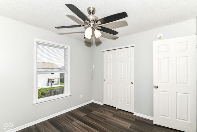 9676 W Constellation Dr, Pendleton, IN 46064 - unfurnished bedroom with dark wood-style flooring, multiple windows, a closet, baseboards, and a textured ceiling