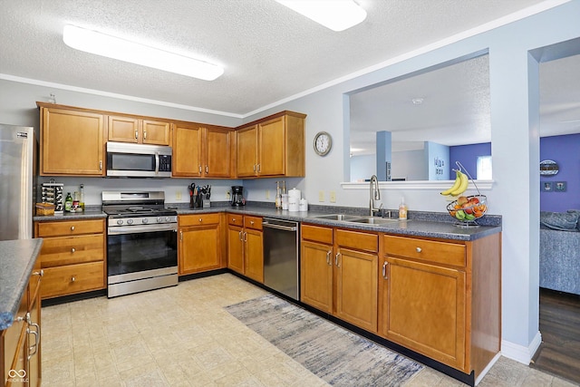 kitchen featuring appliances with stainless steel finishes, a sink, brown cabinetry, a textured ceiling, and dark countertops