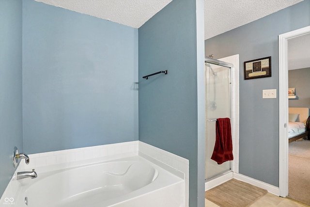 bathroom featuring a shower stall, a textured ceiling, a bath, baseboards, and ensuite bath