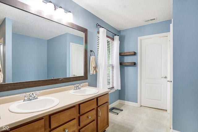 bathroom with a textured ceiling, baseboards, and double vanity