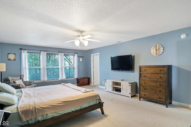 bedroom featuring baseboards, light colored carpet, a ceiling fan, and a textured ceiling