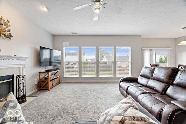 living area with light colored carpet, a textured ceiling, a ceiling fan, a tile fireplace, and baseboards