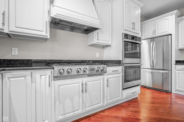 4368 W Eagle Trce, New Palestine, IN 46163 - kitchen featuring stainless steel appliances, premium range hood, white cabinets, wood finished floors, and dark stone counters