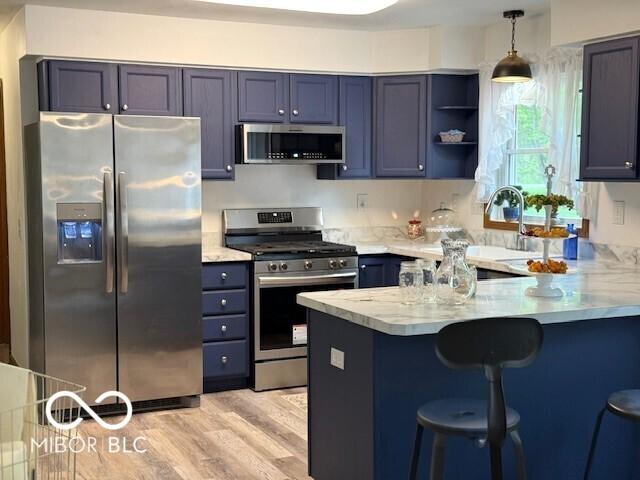 4600 S Tahoe Trl, Crawfordsville, IN 47933 - kitchen featuring appliances with stainless steel finishes, a peninsula, a kitchen breakfast bar, light wood-type flooring, and hanging light fixtures