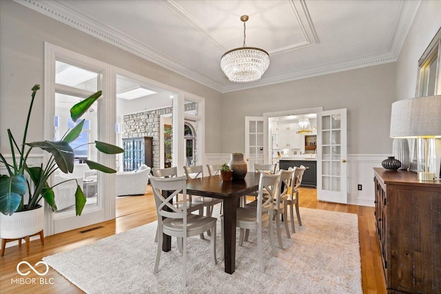 11715 Landings Dr, Indianapolis, IN 46256 - dining area with french doors, a chandelier, crown molding, light wood-type flooring, and wainscoting