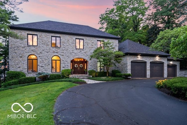 11715 Landings Dr, Indianapolis, IN 46256 - french country style house featuring a garage, stone siding, a yard, and asphalt driveway
