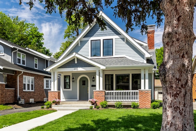 5682 Broadway St, Indianapolis, IN 46220 - view of front facade with covered porch, a front yard, roof with shingles, and brick siding