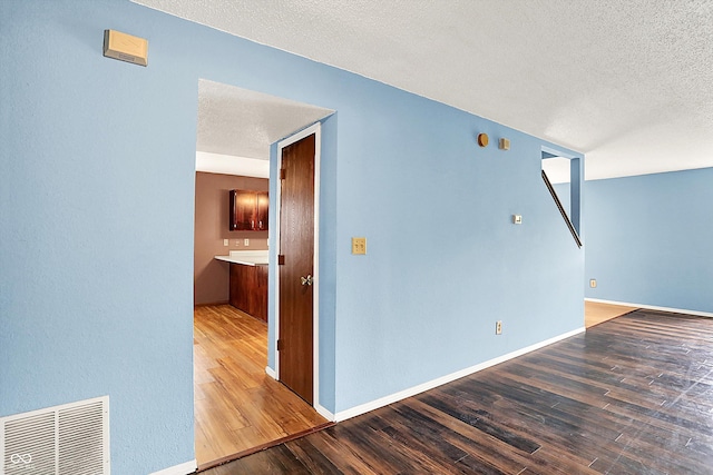 empty room with wood finished floors, a textured ceiling, and baseboards
