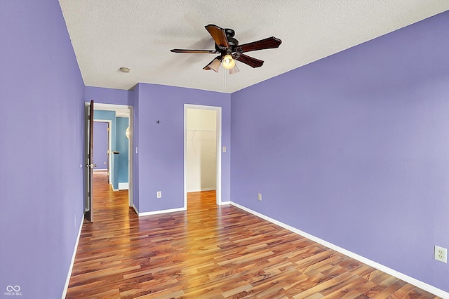 unfurnished bedroom with wood finished floors, a textured ceiling, baseboards, and ceiling fan