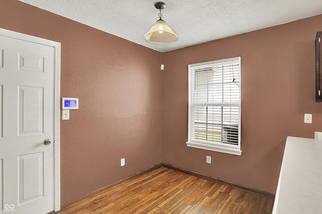 empty room with healthy amount of natural light, wood finished floors, a textured ceiling, and baseboards