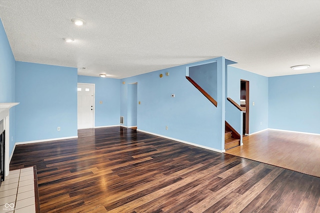 unfurnished living room featuring a textured ceiling, wood finished floors, stairway, a fireplace with flush hearth, and baseboards