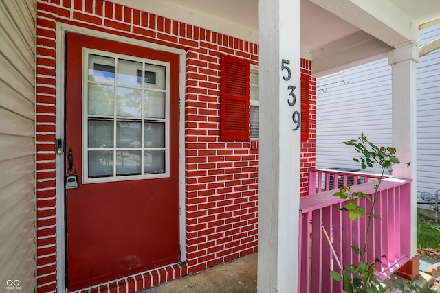 property entrance featuring a porch and brick siding