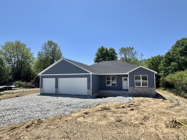ranch-style house featuring an attached garage, stone siding, and gravel driveway