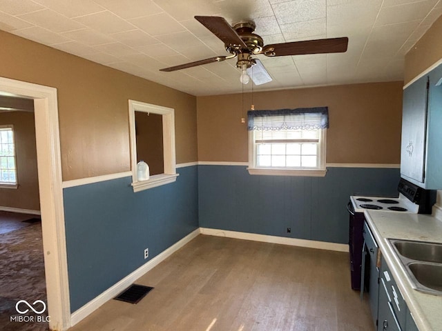 kitchen with healthy amount of natural light, white range with electric stovetop, ceiling fan, wood finished floors, and wainscoting