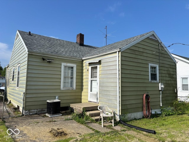 rear view of house with a chimney, central AC, and a shingled roof