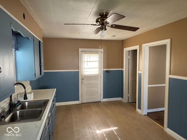 kitchen with a sink, a ceiling fan, wood finished floors, wainscoting, and light countertops