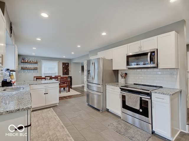 3659 Watson Rd, Indianapolis, IN 46205 - kitchen featuring appliances with stainless steel finishes, a sink, white cabinets, decorative backsplash, and light stone counters