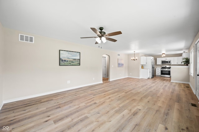 unfurnished living room featuring ceiling fan, light wood finished floors, a chandelier, arched walkways, and baseboards