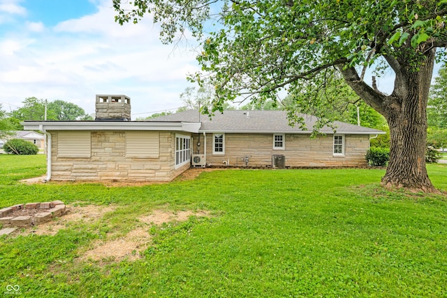 rear view of house with stone siding, central AC unit, a yard, and a chimney