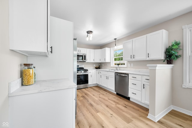 kitchen featuring stainless steel appliances, light wood-style floors, white cabinetry, baseboards, and a sink
