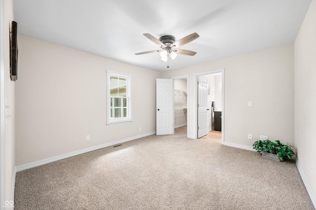 unfurnished bedroom with carpet floors, baseboards, a walk in closet, and ceiling fan