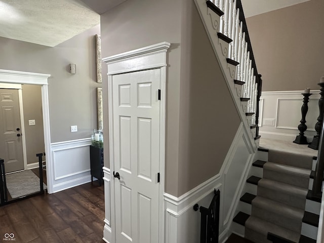 stairway with wood finished floors, a decorative wall, and wainscoting
