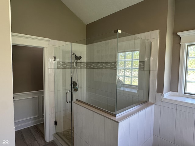 bathroom featuring vaulted ceiling, a stall shower, a decorative wall, a wainscoted wall, and wood finished floors