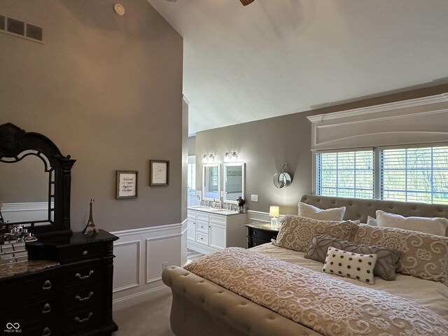 bedroom featuring a wainscoted wall, high vaulted ceiling, a decorative wall, connected bathroom, and carpet flooring