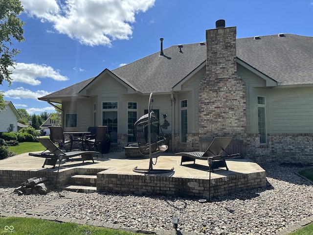 rear view of property with a patio area, a chimney, roof with shingles, and brick siding