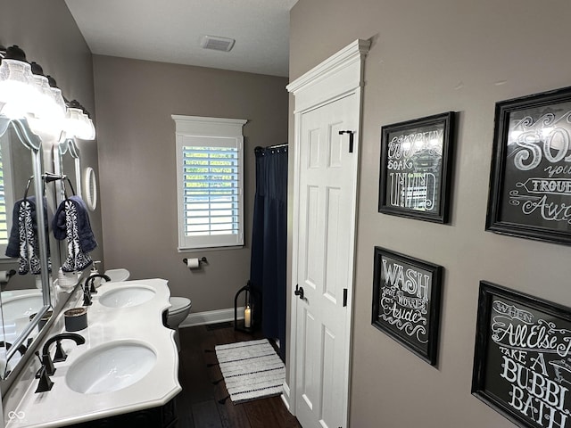 bathroom featuring wood finished floors, toilet, baseboards, and double vanity