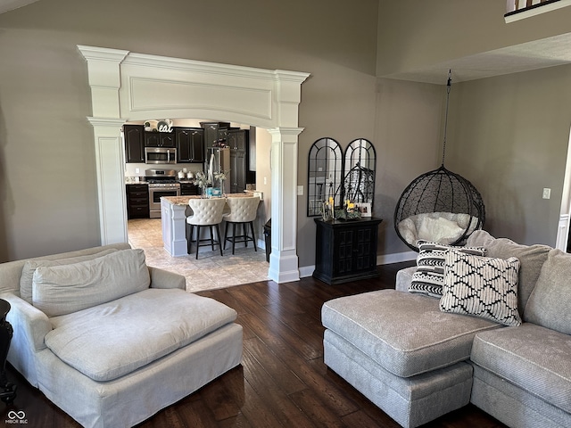 living room with decorative columns, light wood-style flooring, a high ceiling, and baseboards