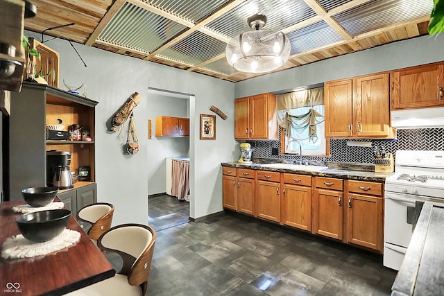 kitchen featuring white gas range oven, under cabinet range hood, a sink, decorative backsplash, and brown cabinetry