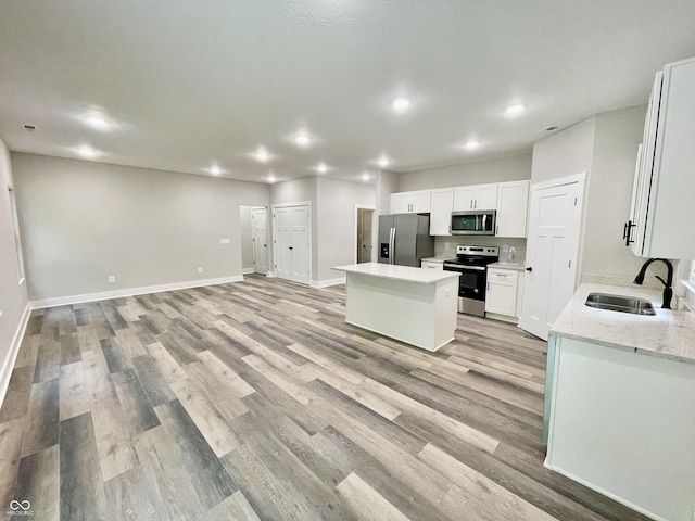 kitchen featuring appliances with stainless steel finishes, a sink, a center island, light wood-style floors, and recessed lighting