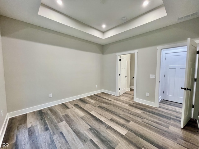 empty room with a tray ceiling, wood finished floors, baseboards, and recessed lighting