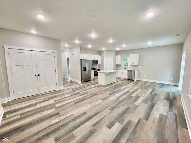 kitchen featuring appliances with stainless steel finishes, open floor plan, white cabinets, light wood finished floors, and baseboards