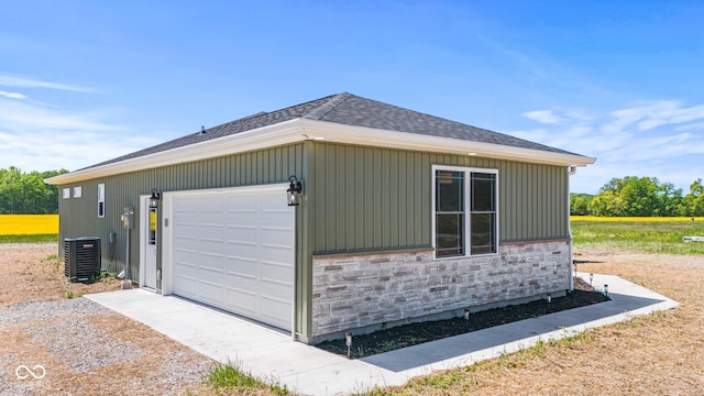 5003 W 900 N, Dupont, IN 47231 - view of side of home with central AC unit, stone siding, a shingled roof, and a garage