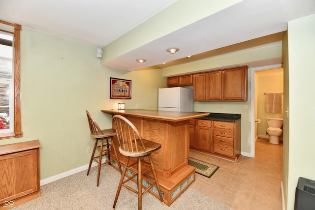 938 Weeping Way Ln, Avon, IN 46123 - kitchen with freestanding refrigerator, brown cabinets, a kitchen bar, baseboards, and a peninsula
