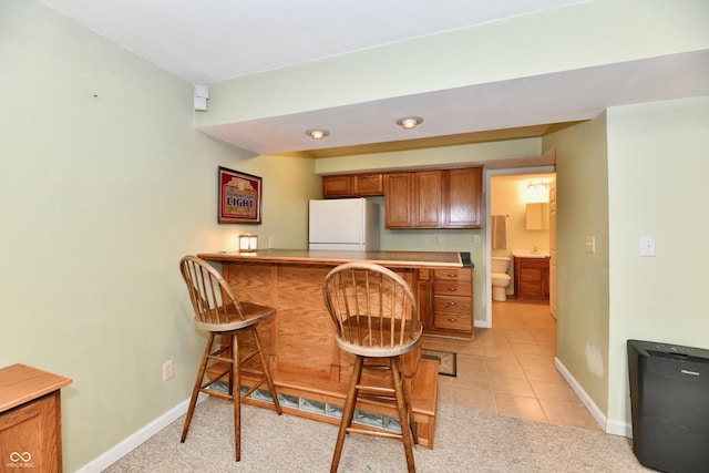 938 Weeping Way Ln, Avon, IN 46123 - kitchen featuring freestanding refrigerator, brown cabinetry, a kitchen bar, and baseboards