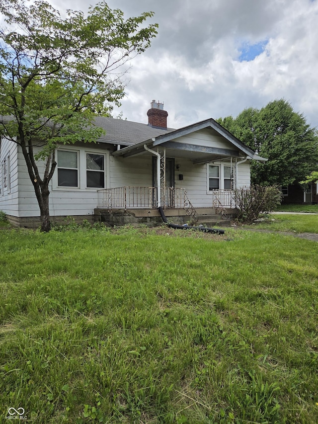 1168 N Gladstone Ave, Indianapolis, IN 46201 - view of front facade with a chimney, covered porch, a front yard, and a shingled roof