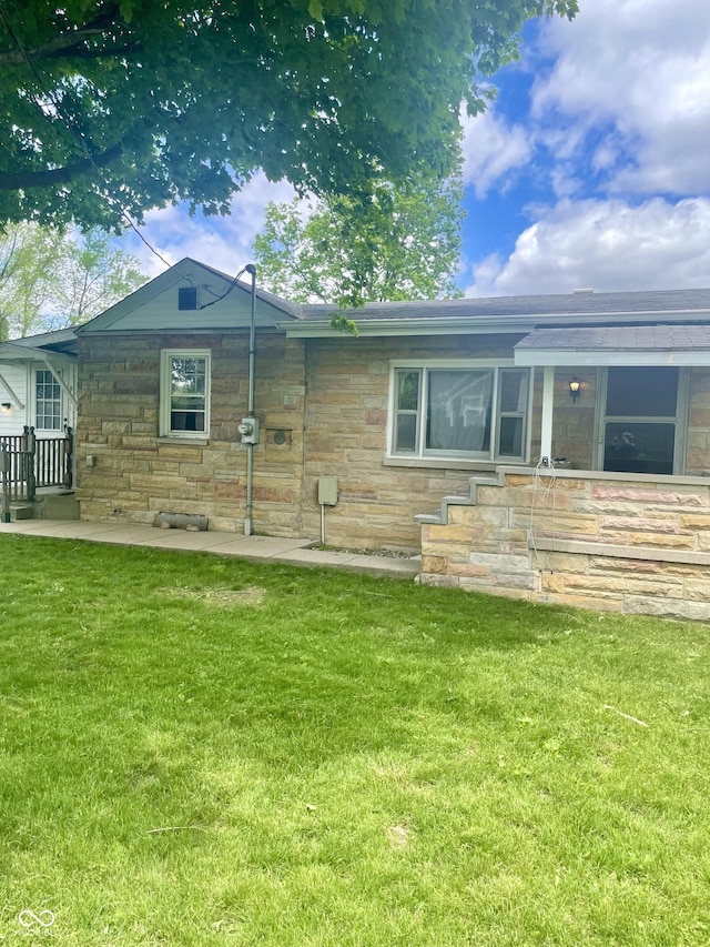 back of house featuring stone siding and a lawn