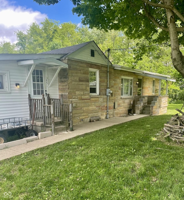 back of house featuring stone siding and a lawn