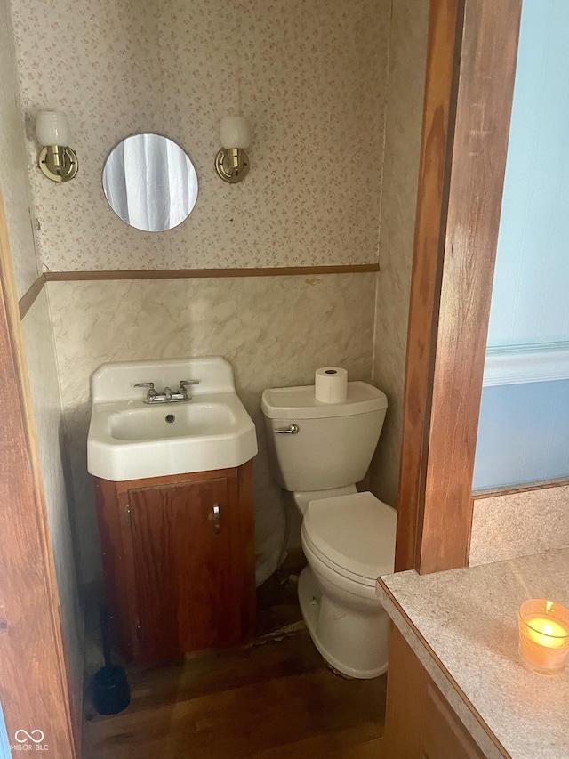 bathroom featuring vanity, wallpapered walls, toilet, and wood finished floors