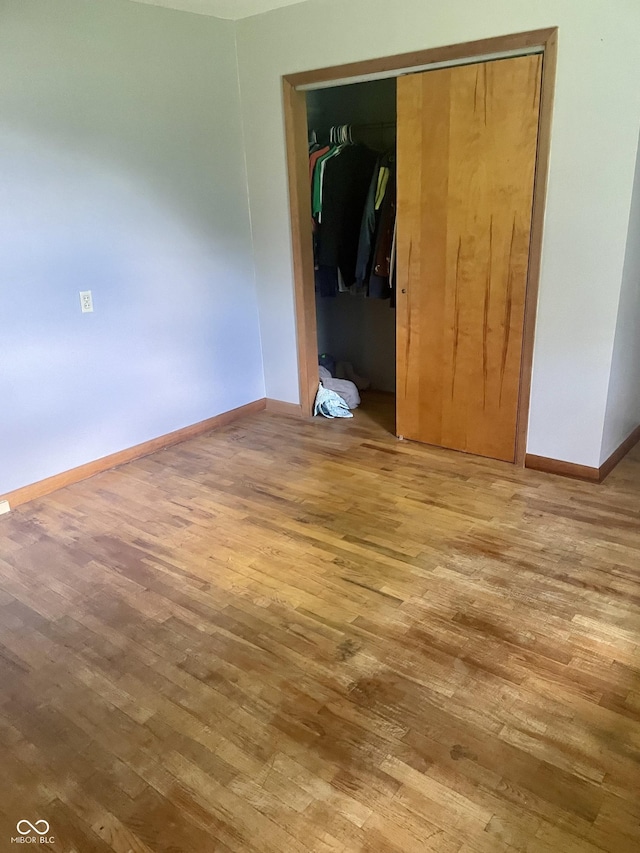 unfurnished bedroom with wood finished floors, baseboards, and a closet