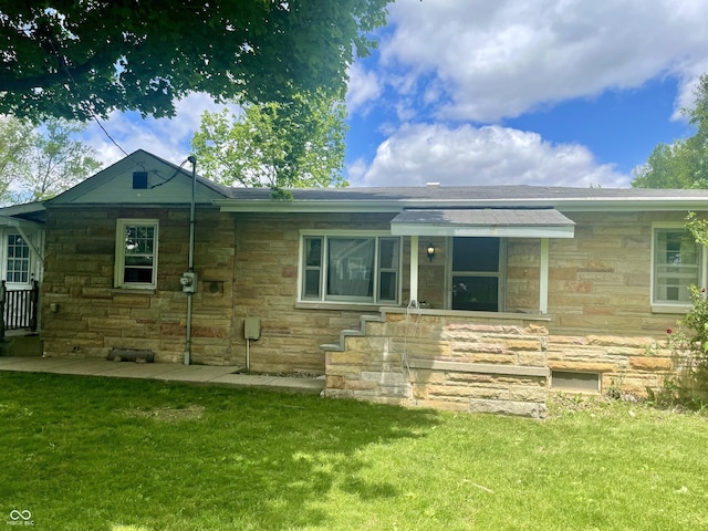 back of house with stone siding and a lawn