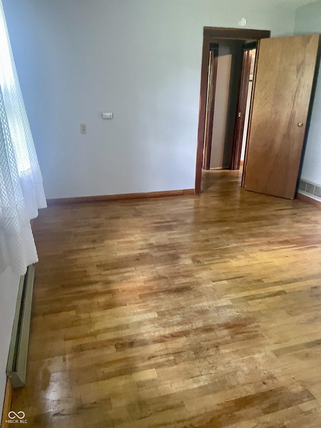 empty room featuring a baseboard heating unit, wood finished floors, and baseboards