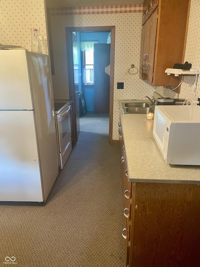 kitchen featuring white appliances, a sink, wallpapered walls, carpet, and light countertops