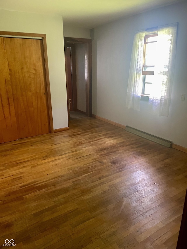 spare room with wood finished floors, a baseboard radiator, and baseboards