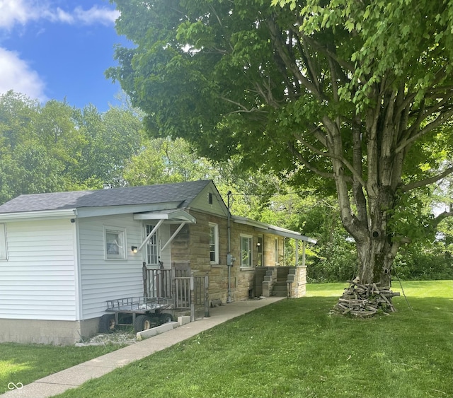 view of side of property featuring a yard, a shingled roof, and stone siding