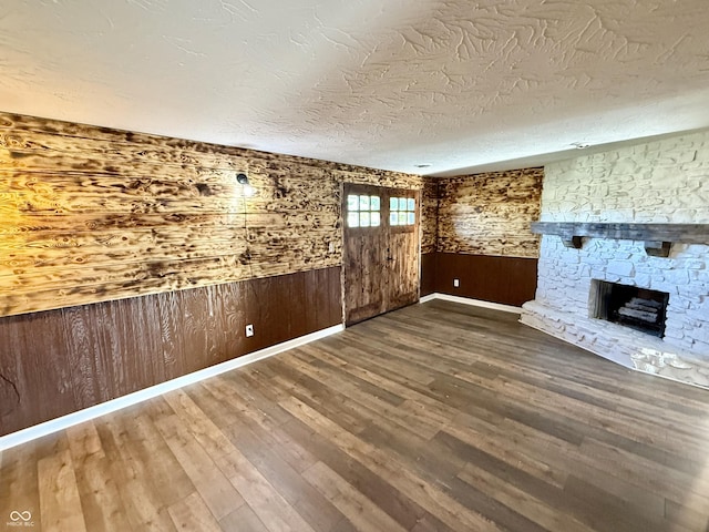 1328 N 300 E, Anderson, IN 46012 - unfurnished living room featuring wood walls, a fireplace, wood finished floors, baseboards, and a textured ceiling